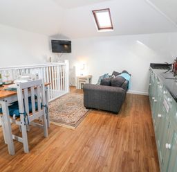 An open plan kitchen and living area with a dining table set for two a sofa and a wall mounted television at The Bath House in Blockley