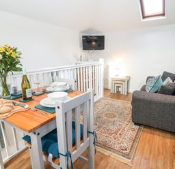 A dining table set with plates glasses bread and wine next to a gray sofa with cushions and a rug in a living area at The Bath House in Blockley