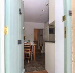 View through an open front door into a kitchen dining area with a table set for breakfast and a staircase in the background at Red Fawn Cottage in Blockley