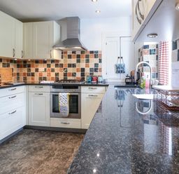 A kitchen with white cabinets a tiled backsplash a stove a microwave and a countertop at Red Fawn Cottage in Blockley