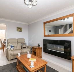 A living room with a beige sofa wooden coffee table side tables a wall-mounted fireplace and a large mirror at Beach View House in Wyke Regis