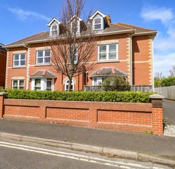 A two story brick residential building with dormer windows and a hedge in front at Marina Reach in Weymouth