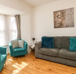 A living room with two teal armchairs and a grey sofa with cushions and a Buddha painting on the wall at Marina Reach in Weymouth