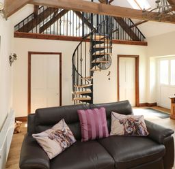 A living room with a brown leather sofa with animal print cushions a spiral staircase and wooden beams at The Old Dairy in Maenclochog