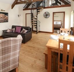 A living room with a dining table set for four and a spiral staircase at The Old Dairy in Maenclochog
