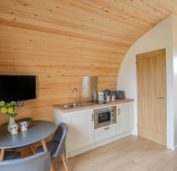 A small kitchen area with a sink microwave and toaster next to a round table with chairs and a wall-mounted TV at Caban Cariad in Bryngwran near Bodedern