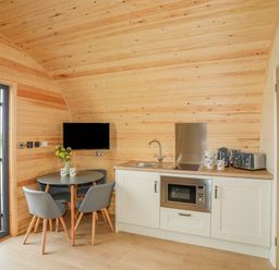 A small kitchen area with a round table and chairs a microwave an electric stove kettle and toaster at Caban Cariad in Bryngwran near Bodedern
