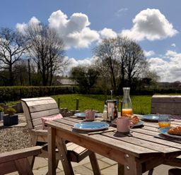 A garden with a wooden table set for breakfast at Pensarngerrig in Rhydlewis