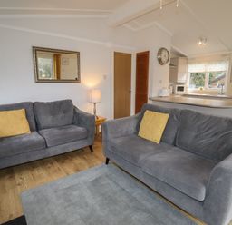 A living room with two grey sofas and yellow cushions next to a kitchen with a countertop at Wayside Lodge in Aston On Clun