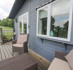 An outdoor wooden deck with wicker chairs and a table outside a blue building at Wayside Lodge in Aston On Clun