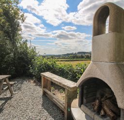 An outdoor fireplace and wooden seating area in a garden at Aston - Shepherd Hut Aston On Clun