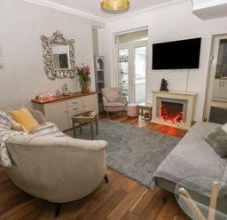 A living room with sofas, a coffee table, a wall mirror, a television above an electric fireplace and a doorway leading to a kitchen at 5 Pontardulais Road in Llangennech