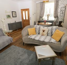 A living room with a curved sofa, yellow pillows, a small table, and a dining table by the window at 5 Pontardulais Road in Llangennech