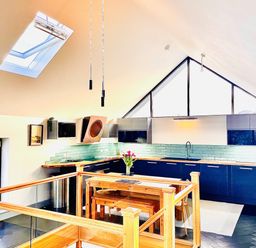 A kitchen with blue cabinets wooden countertops and a wooden dining table with flowers at Avalennek in St Newlyn East