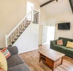 A living room with two sofas a wooden coffee table a wall mounted tv a staircase with wrought iron railing at Y Bwthyn Bach in Tregarth