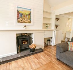 A living room with a wood-burning stove fireplace a gray sofa with a colorful cushion and a painting above the fireplace at Y Bwthyn Bach in Tregarth