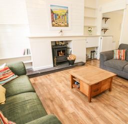 A living room with two sofas a wooden coffee table and a fireplace with fire burning at Y Bwthyn Bach in Tregarth