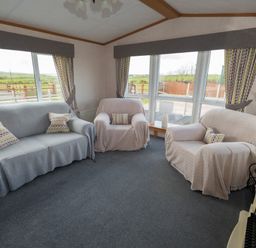 A living room with sofas armchairs cushions curtains and large windows at The Lodge in Rhosybol