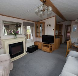 A living room with a fireplace a television a dining table and chairs at The Lodge in Rhosybol