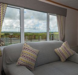 A living room with a sofa and patterned cushions in front of large windows with a view of fields at The Lodge in Rhosybol