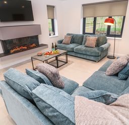 A living room with teal sofas a coffee table with snacks a fireplace and a wall mounted tv at Tredarn in Connor Downs