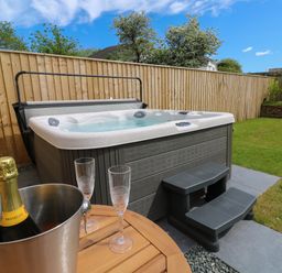 A garden with a hot tub table with champagne and glasses and wooden fencing at Tredarn in Connor Downs