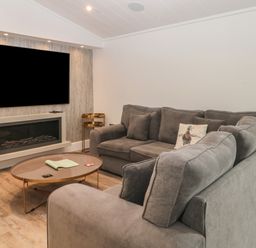 A living room with a gray sectional sofa a round coffee table a wall-mounted television and a fireplace at Ruperts Retreat in Nateby near Garstang
