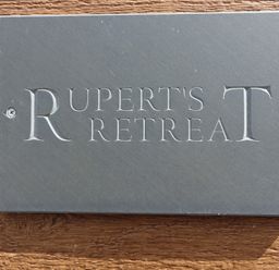 A rectangular stone sign with the words Ruperts Retreat engraved mounted on a wooden surface at Ruperts Retreat in Nateby near Garstang