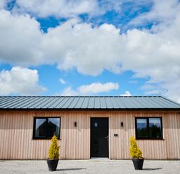 Front view of a wooden building with two windows a black door and two potted plants at Ingleborough Lodge in Rathmell near Settle