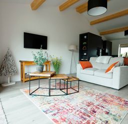 A living room with a light gray sofa and orange cushions a wooden coffee table and a colorful rug at Ingleborough Lodge in Rathmell near Settle