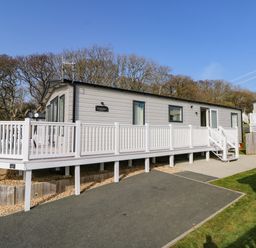 A static caravan with a white deck railing and steps surrounded by trees at Crosswinds 68 in Bembridge