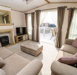 A living room with two sofas a pouf tv and a fireplace with mirror at Crosswinds 68 in Bembridge