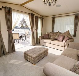 A living room with two sofas an ottoman and patio doors leading to a deck at Crosswinds 68 in Bembridge