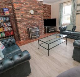 A living room with blue leather sofas a glass coffee table a brick fireplace and a bookshelf at Barnacre in Longhirst near Morpeth