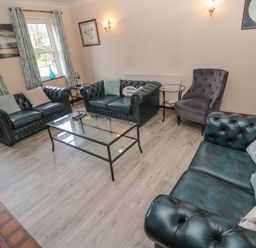 A living room with dark leather sofas a glass coffee table an accent chair and curtains at Barnacre in Longhirst near Morpeth