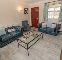 A living room with two leather sofas a glass coffee table an armchair wall sconce and a window with curtains at Barnacre Longhirst near Morpeth