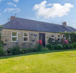 A stone house with a slate roof surrounded by plants and flowers in a garden at Barnacre in Longhirst near Morpeth
