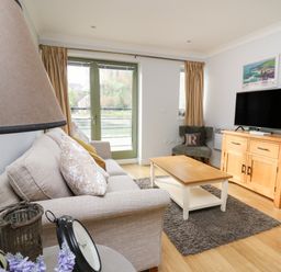 A living room with a sofa cushions wooden coffee table and television on a wooden cabinet at Flat 2 in Pembroke