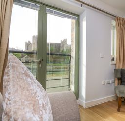 A living room with a sofa and chair near a glass door showing a castle outside at Flat 2 in Pembroke