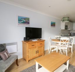 A living area with a wooden cabinet holding a TV a round dining table with four chairs a couch with cushions and a wooden coffee table at Flat 2 in Pembroke