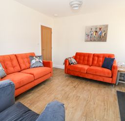 A living room with two orange sofas, a blue chair, a wooden door, and a painting of zebras at The Chocolate Box in Weymouth