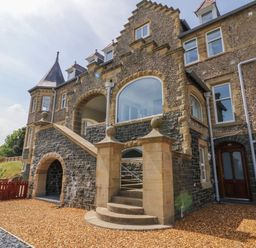 The exterior of a stone building with arched windows and a staircase leading to an upper level at On the Straits in Glyngarth near Menai Bridge