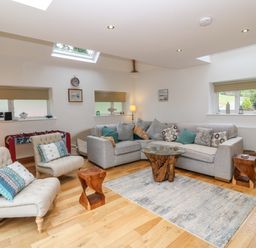 A living room with a grey sectional sofa two beige armchairs a glass and wood coffee table and wooden stools at On the Straits in Glyngarth near Menai Bridge
