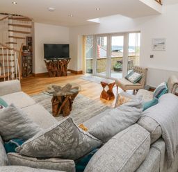 A living room with a spiral staircase a glass top table with wooden base a television two armchairs and a large sofa at On the Straits in Glyngarth near Menai Bridge