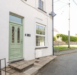 The exterior of a house with a light green door and a window on a paved sidewalk at Gwel Y Mor in Beaumaris