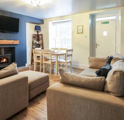 A living room with beige sofas wooden dining table with six chairs a fireplace and a wall-mounted television at Gwel Y Mor in Beaumaris