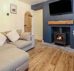 A living room with a beige sofa, a wood-burning stove in a blue fireplace, a mounted TV, and a wooden door at Gwel Y Mor in Beaumaris