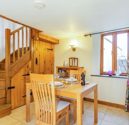 A dining area with a wooden table and chairs next to stairs and a window at Miller's Lodge in St Keyne near Liskeard