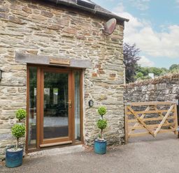 Entrance door in a stone building with two potted plants and a wooden gate at Miller's Lodge in St Keyne near Liskeard