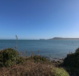 A coastal view showing the sea with vegetation and hills in the background at Sandpiper in Weymouth
